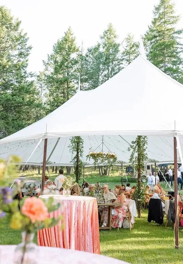 Cocktail table in a coral cloth in front of a peaked white tent on a lawn lined with pine trees