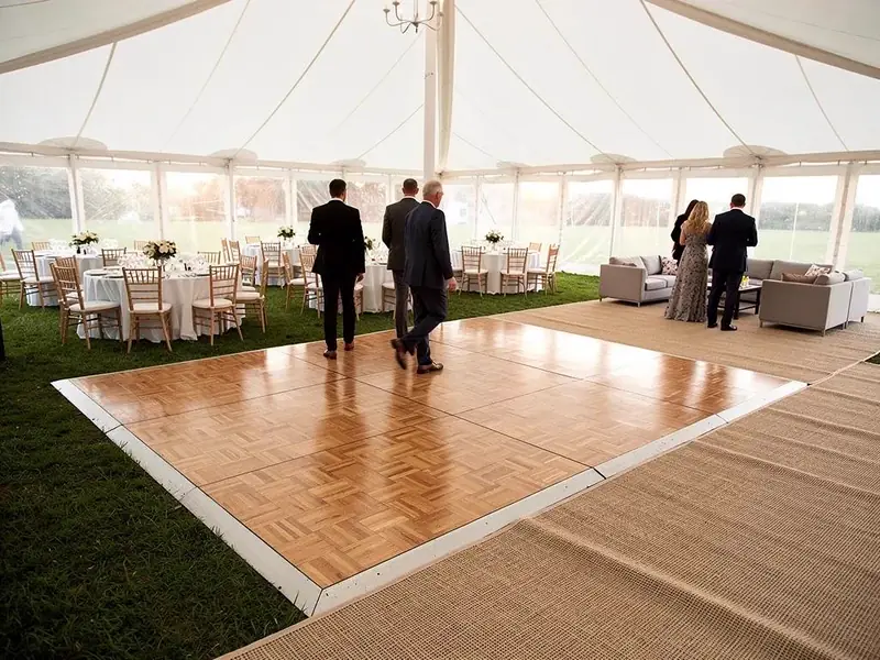Wood dance floor, round tables, a gray lounge set and a chandelier inside a white frame tent