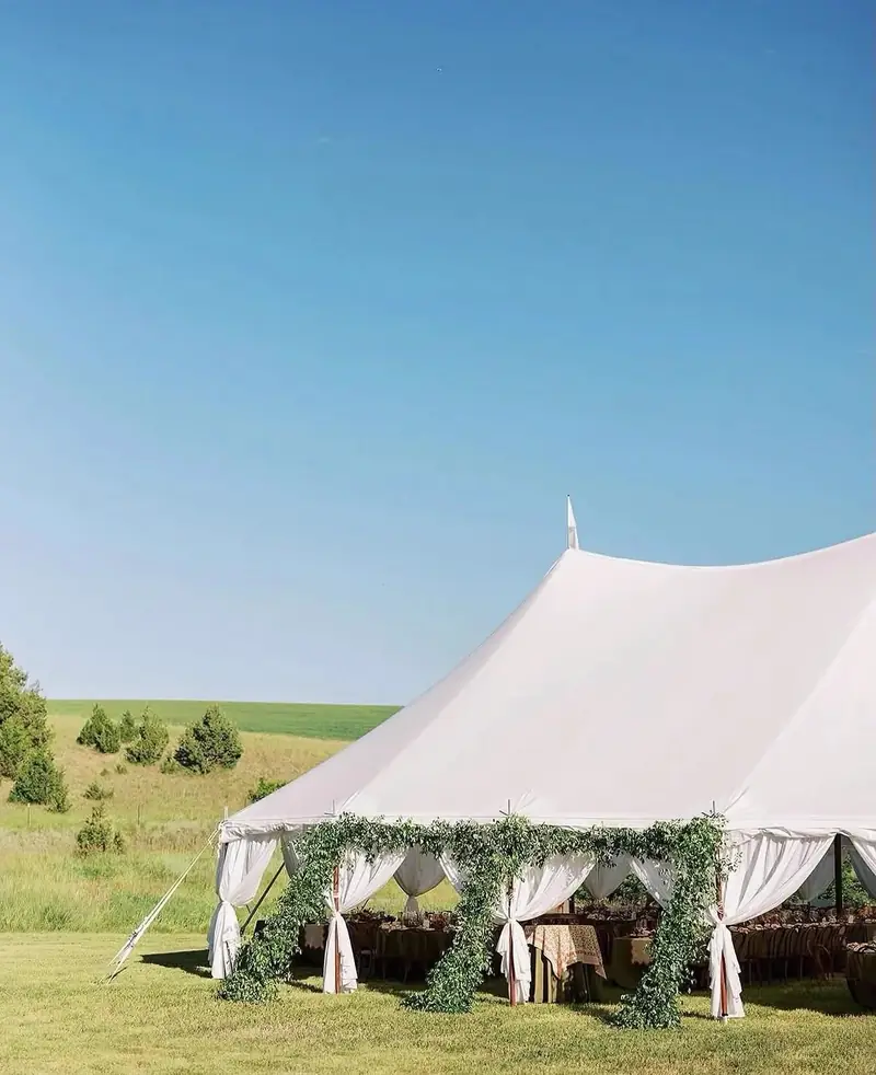 High-peak white tent with a greenery garland along the front on a field with green hills