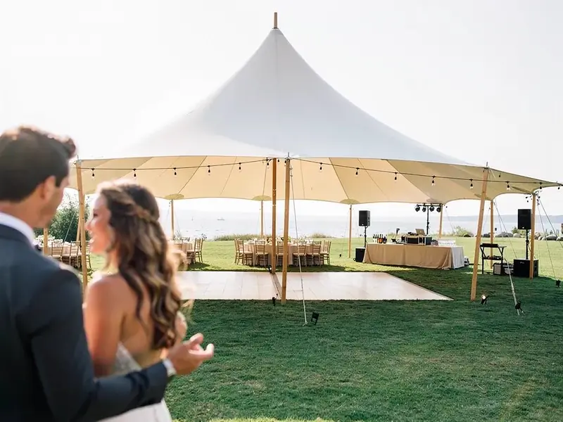 Sailcloth tent with a dance floor, long tables and speakers on a lawn beside a lake