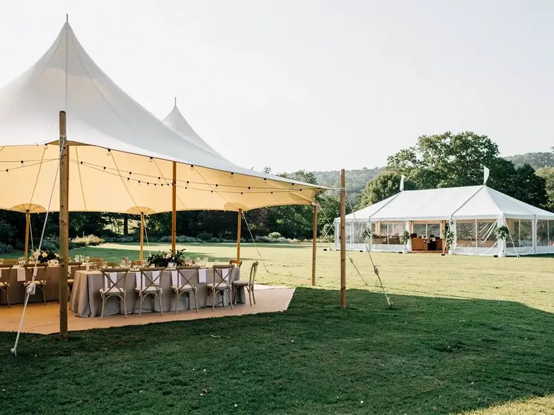 Sailcloth tent over a wood deck with tables and string lights beside a white frame tent