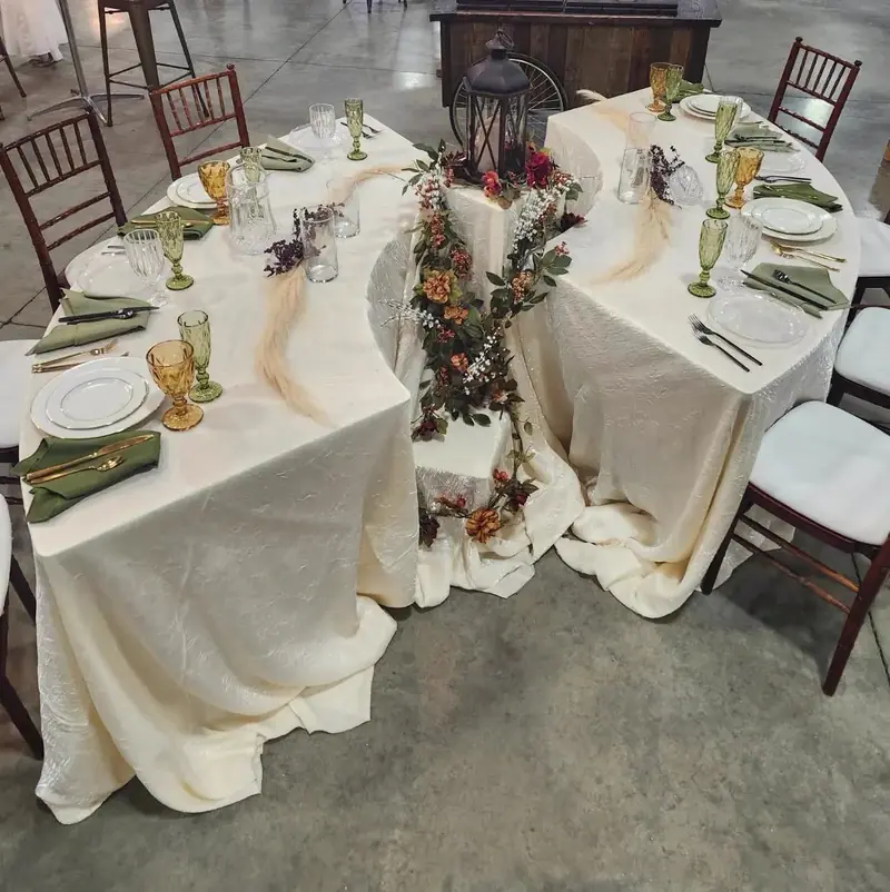 Overhead view of a curved serpentine table with an ivory cloth, greenery runner and dark wood chairs