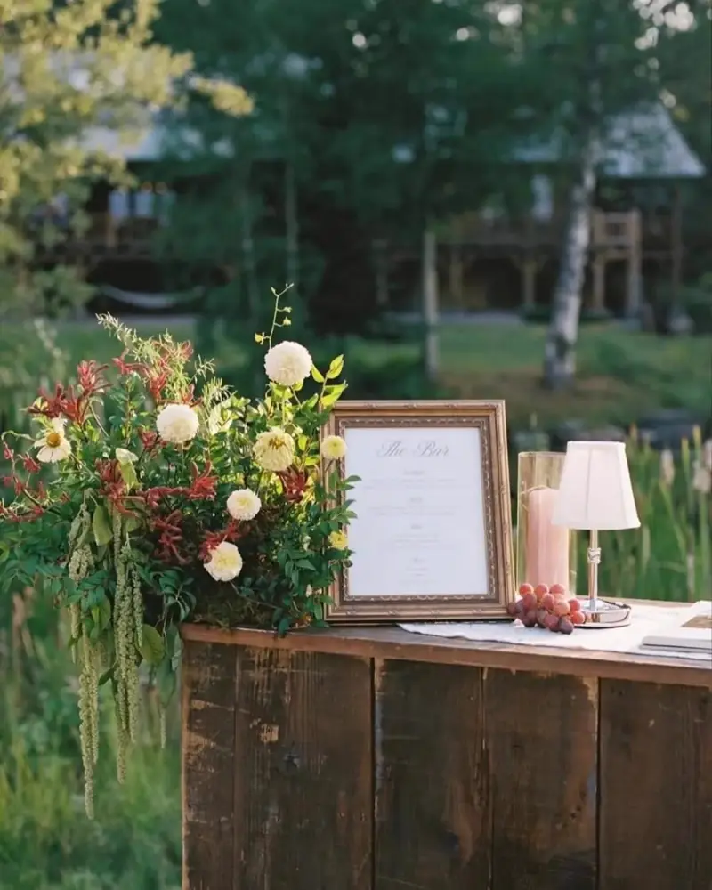 Dark wood bar top with a framed sign and a burgundy and yellow flower arrangement outdoors