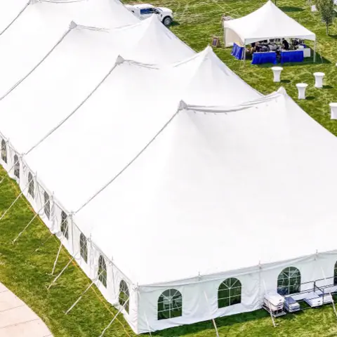 A large white event tent on a green lawn seen from above, with cocktail tables set nearby