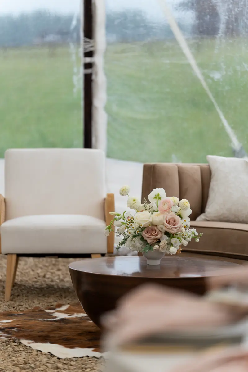 A cream armchair, a brown sofa and a dark wood coffee table on a brown and white cowhide rug