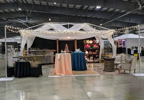 An event booth built with sheer white drapes, fairy lights, cocktail tables in peach and blue linens, and armchairs
