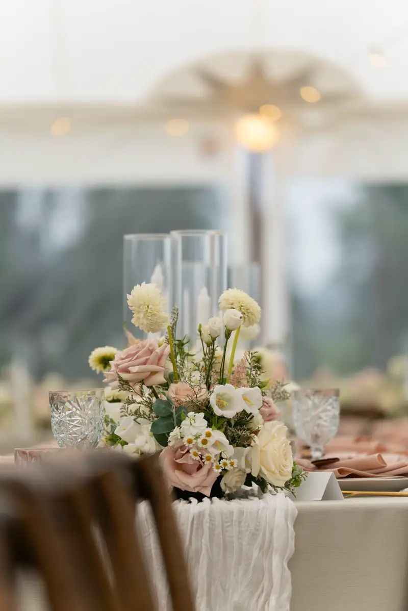 A white gauze runner and blush napkins down a long beige dressed table with candles
