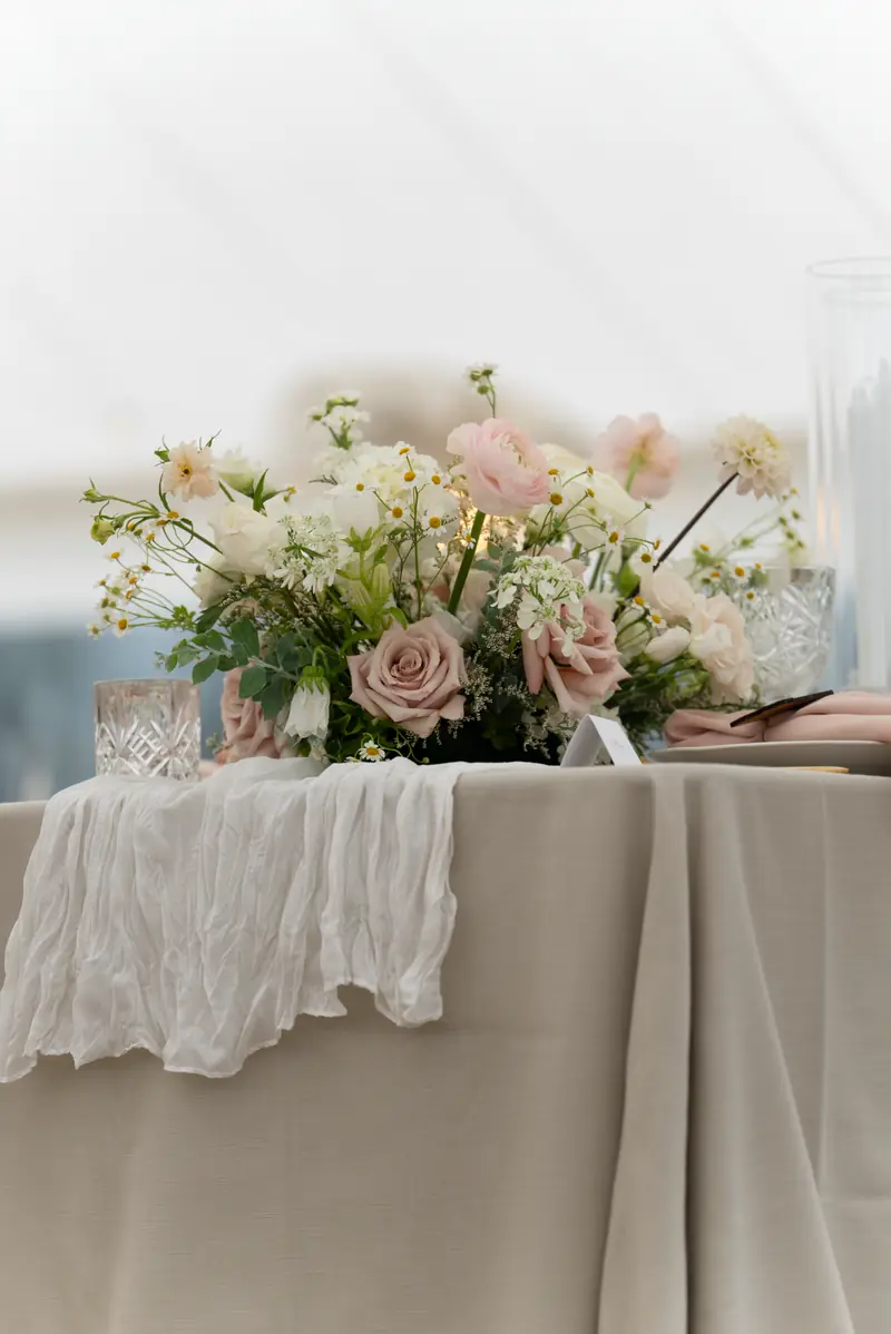 A beige tablecloth under a sheer gauze runner with pink, cream and white flowers