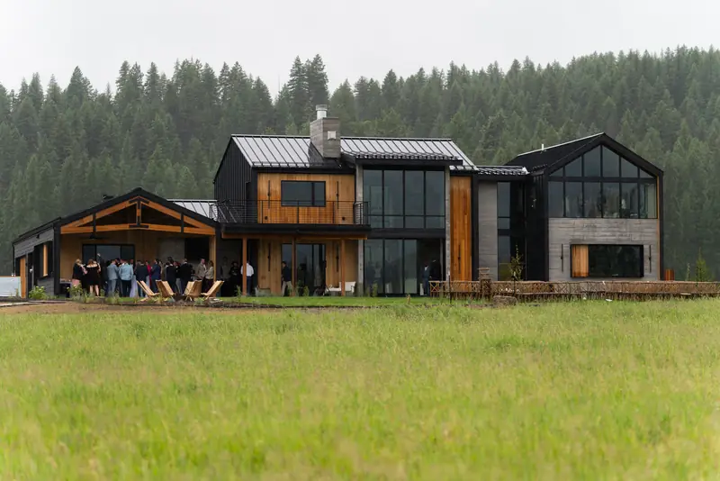 Guests gathered outside a modern wood and glass house at the edge of dense woods