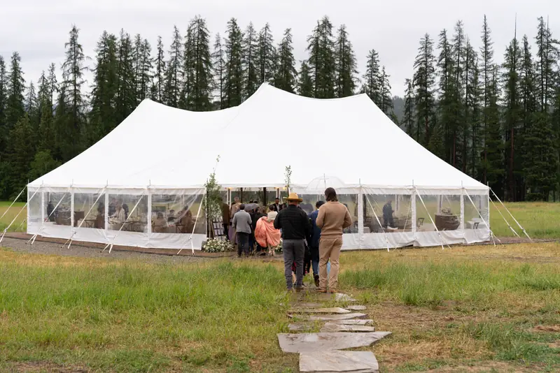 Guests walk a stone path toward a large white tent with clear walls on an overcast day
