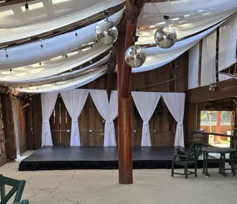 A low stage under white ceiling drapes with disco balls hanging above an event floor