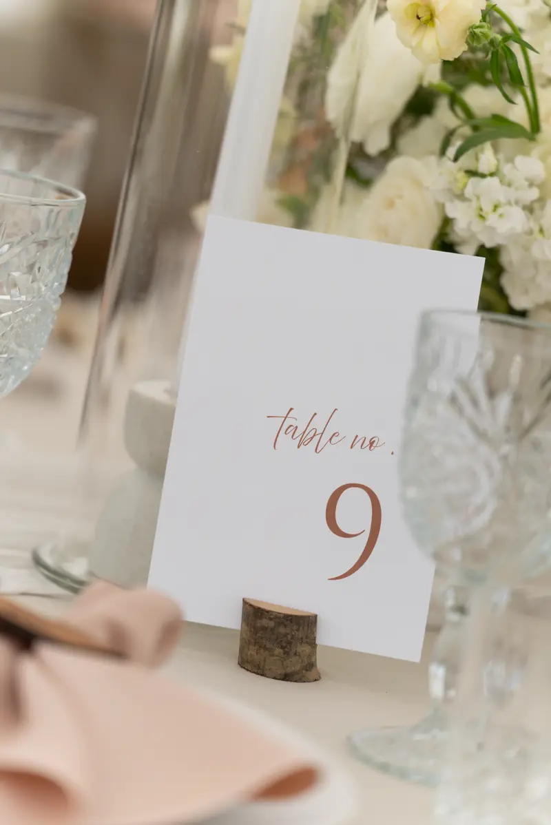 A table number nine card in a small wood stand beside crystal glasses and folded blush napkins