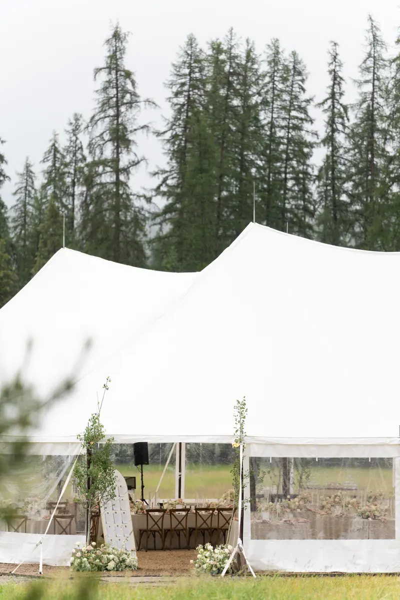 The entrance of a white wedding tent decorated with flowers beside tall trees, shot in portrait