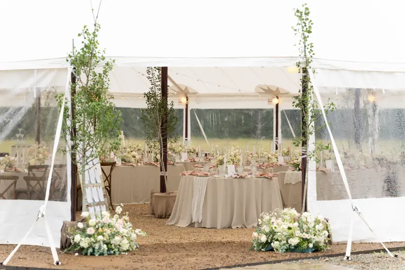A view into an open tent showing floral arrangements, dressed tables and a gravel floor