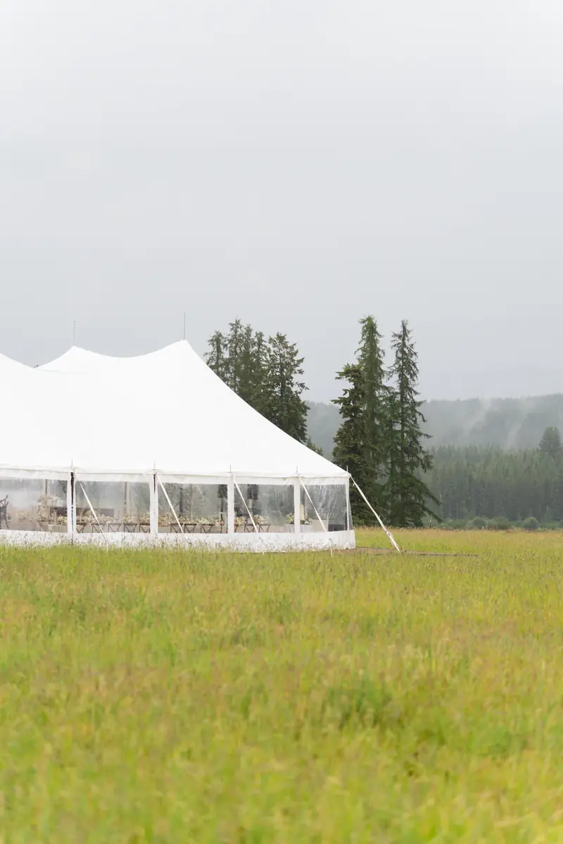 A white outdoor event tent set up on a grassy meadow, shot in portrait