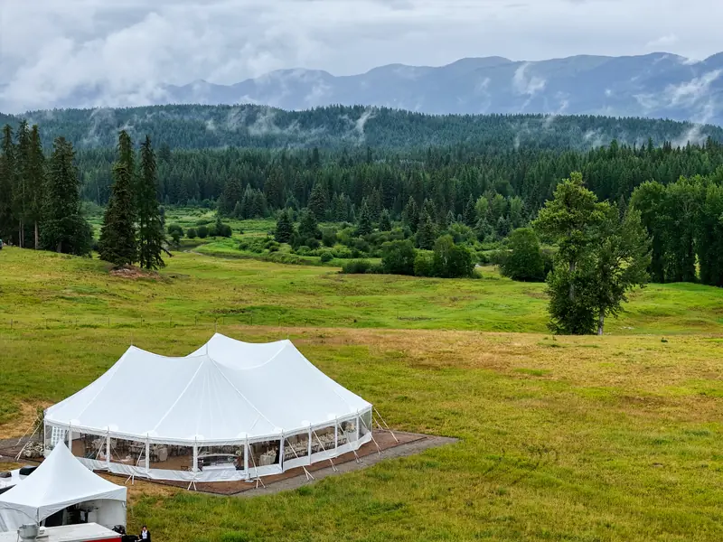 A wide raised view of a white event tent set among rolling green hills and forest