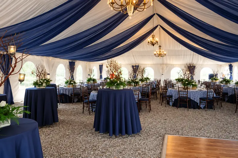 A wood plank dance floor in a tent with navy and white ceiling drapes and three hanging chandeliers