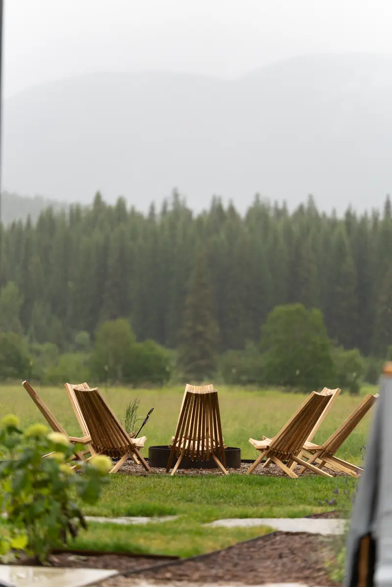 Wooden outdoor lounge chairs arranged in a circle on a lawn with a forest behind